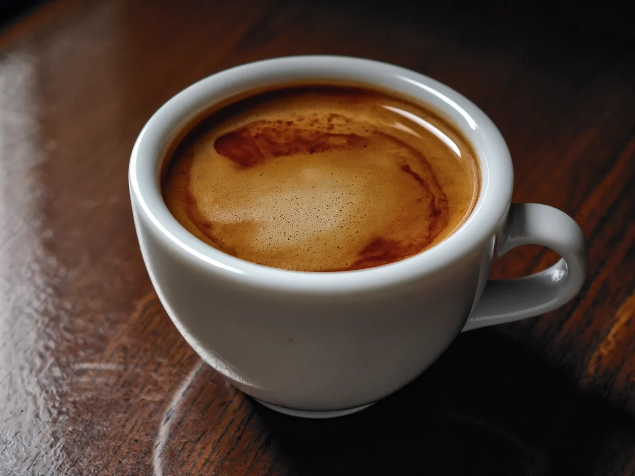 Espresso dublu cu crema aurie, într-o ceașcă albă, pe blat de lemn.