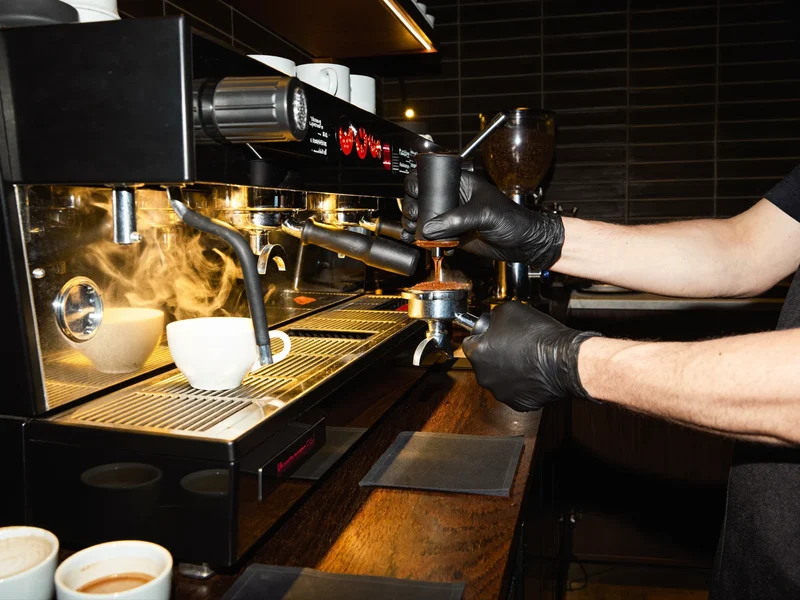 Mâinile unui barista presează cafeaua măcinată în portafiltru la aparatul de espresso.
